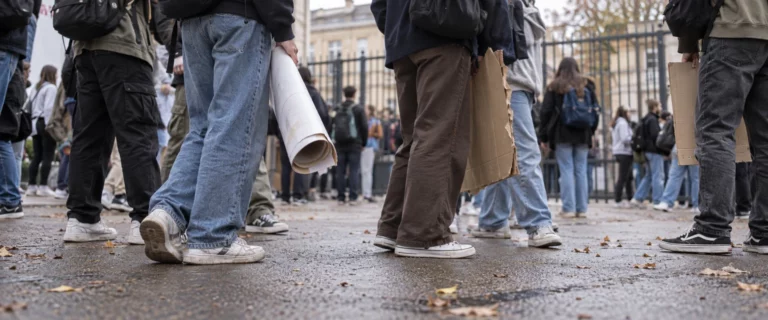 Pancartes portées à hauteur des jambes et baskets de lycéens rassemblés devant un portail, vus au ras du sol.